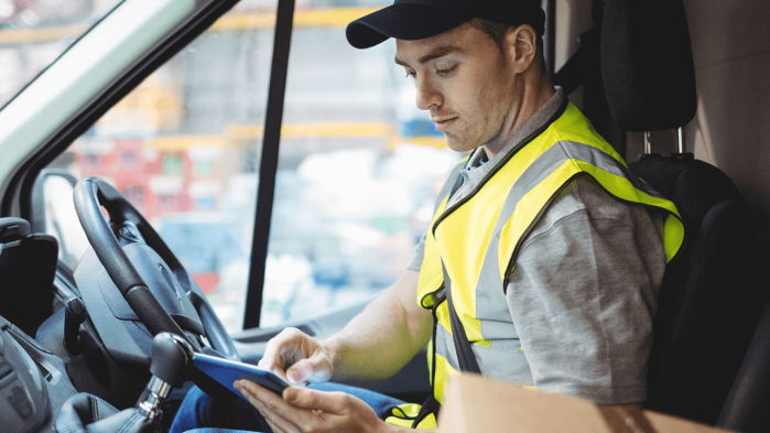 Ein Lieferfahrer in Warnweste nutzt ein Tablet im Lieferwagen, um Kommunikation effizient zu überbrücken.