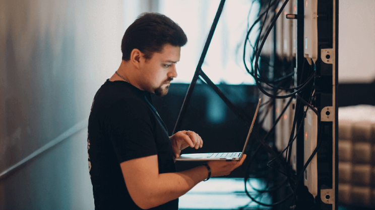 Ein Systemadministrator arbeitet neben digitaler Infrastruktur an seinem Laptop