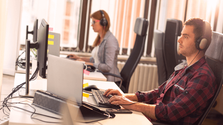 Zwei Systemadministratoren sitzen mit aufgesetztem Headset an ihren Computern in einem Büro