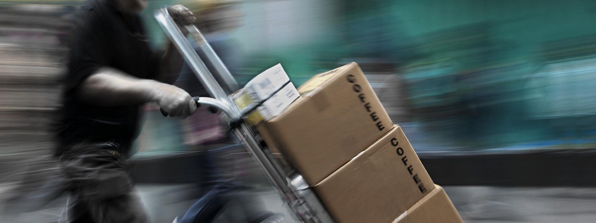 Paketbote transportiert drei braune Kartons auf einem Sackkarren.