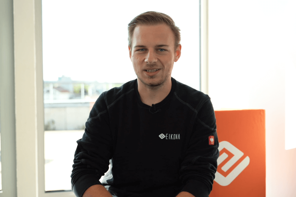Ein Auszubildender in einem Büro, der einen schwarzen Pullover mit dem Logo von EIKONA Logistics trägt.