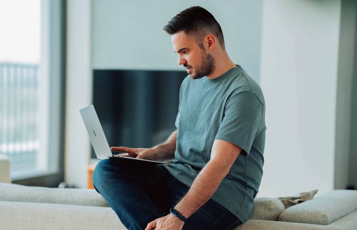 Mitarbeiter sitzt mit seinem Laptop auf der Couch im Homeoffice und mindert die Cybergefahren da er durch Wissen und Sorgfalt vorbereitet ist