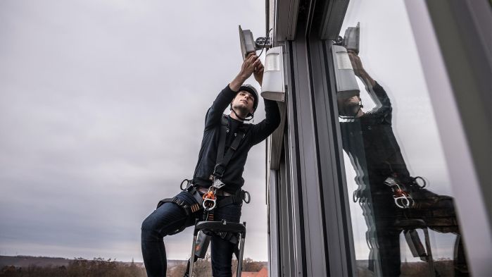Techniker installiert an Außenfassade einer Logistikhalle WLAN-Komponenten