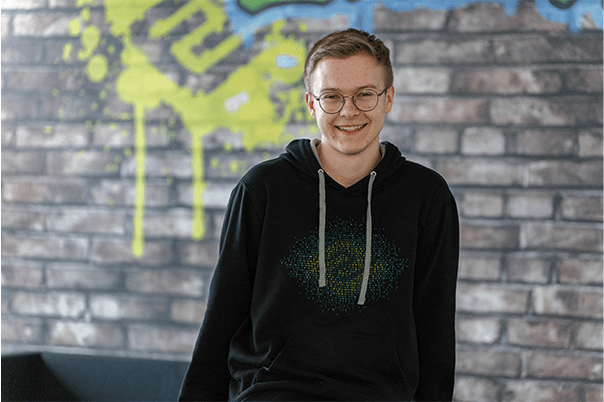 Junger Mann im schwarzen Pullober lächelt in die Kamera.