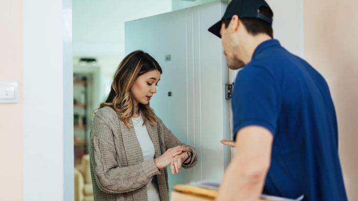 Endkundin schaut auf Uhr, weil Lieferung nicht automatisch avisiert wurde und zu spät kommt.