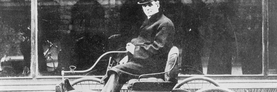 Black and white photo of Henry Ford on a historic car model