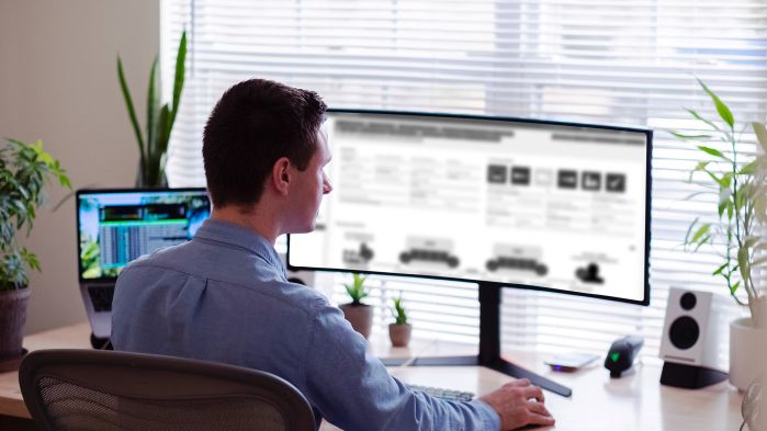 Mann sitzt an seinem Schreibtisch und schaut auf den Monitor seines Computers