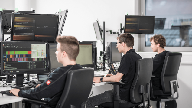 Drei Mitarbeiter arbeiten an ihren Arbeitsplätzen vor Bildschirmen.
