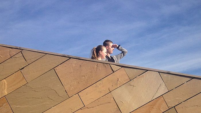 Ein junges Paar steht hinter einer Mauer und blickt in die Ferne.