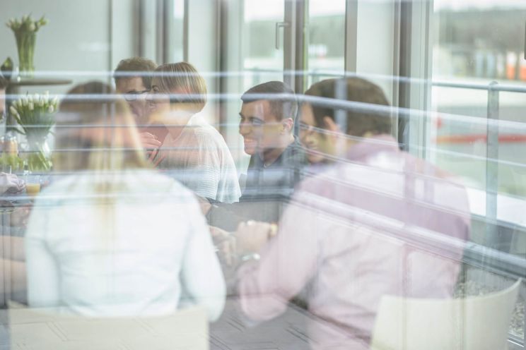 Through a pane of glass you can see six people sitting together at the table, smiling.