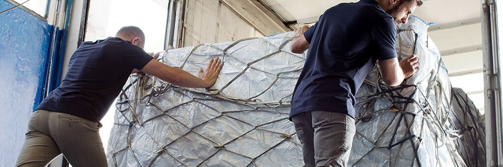 Two logistics employees secure general cargo shipments on a loading area – a symbol of efficient and digital general cargo logistics in modern logistics networks.