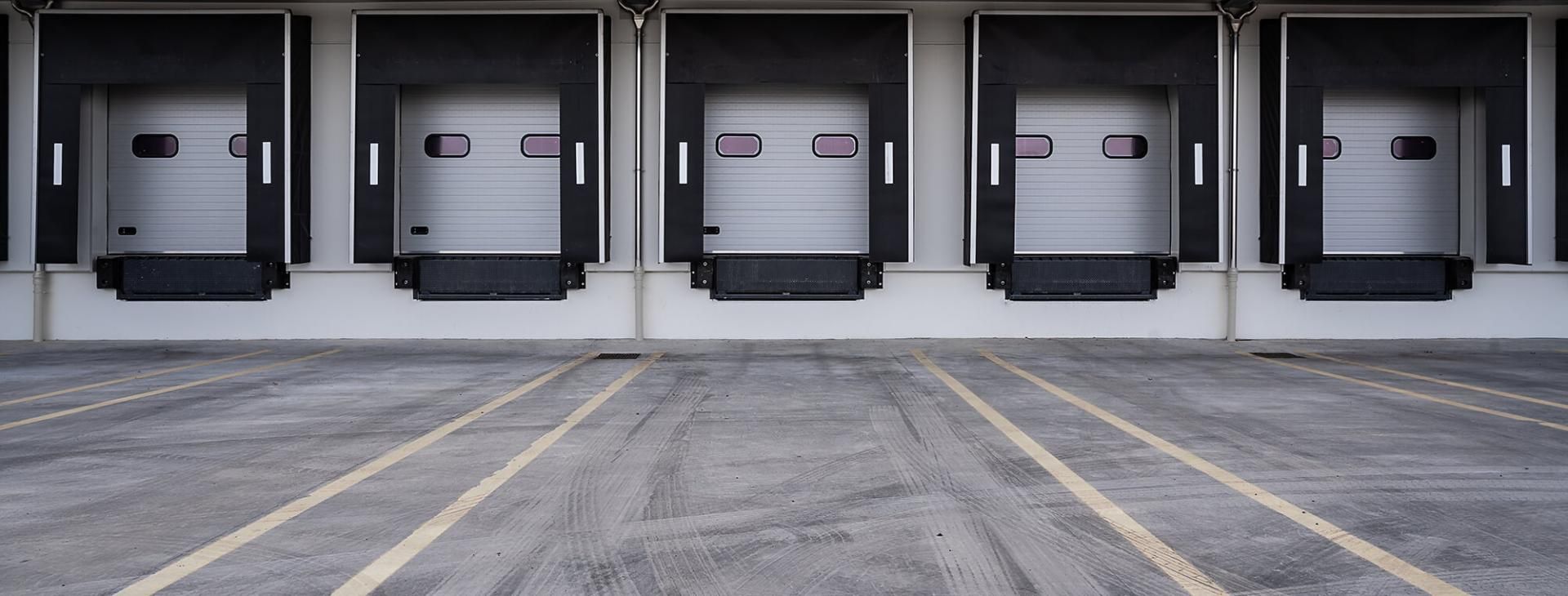 Die EIKONA Logistics Cloud steuert Versandprozesse von Verladern. Fünf weiße Verladerampen einer Lagerhalle.