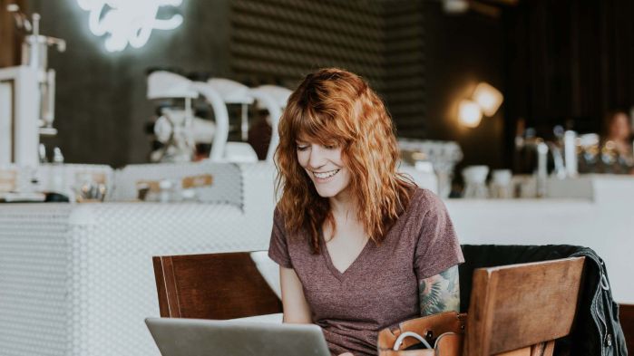 Woman with red hair sits at a table and works with her laptop in a cafe using desktop virtualization