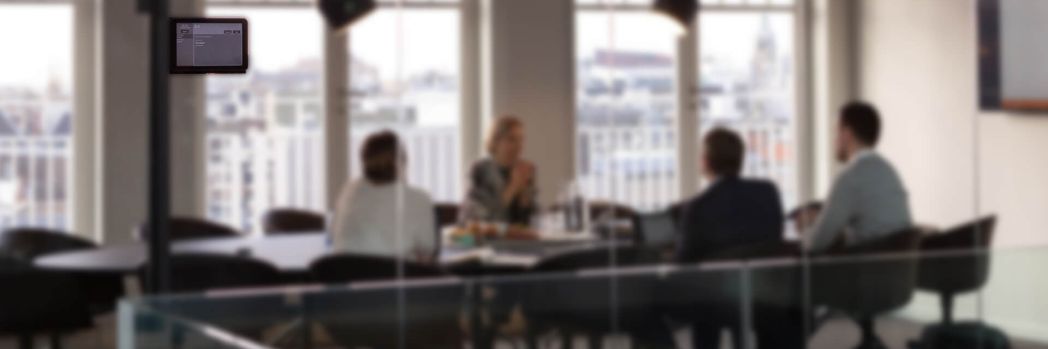 Employees sitting at meeting table in meeting room which is signposted with Wireless ePaper Display