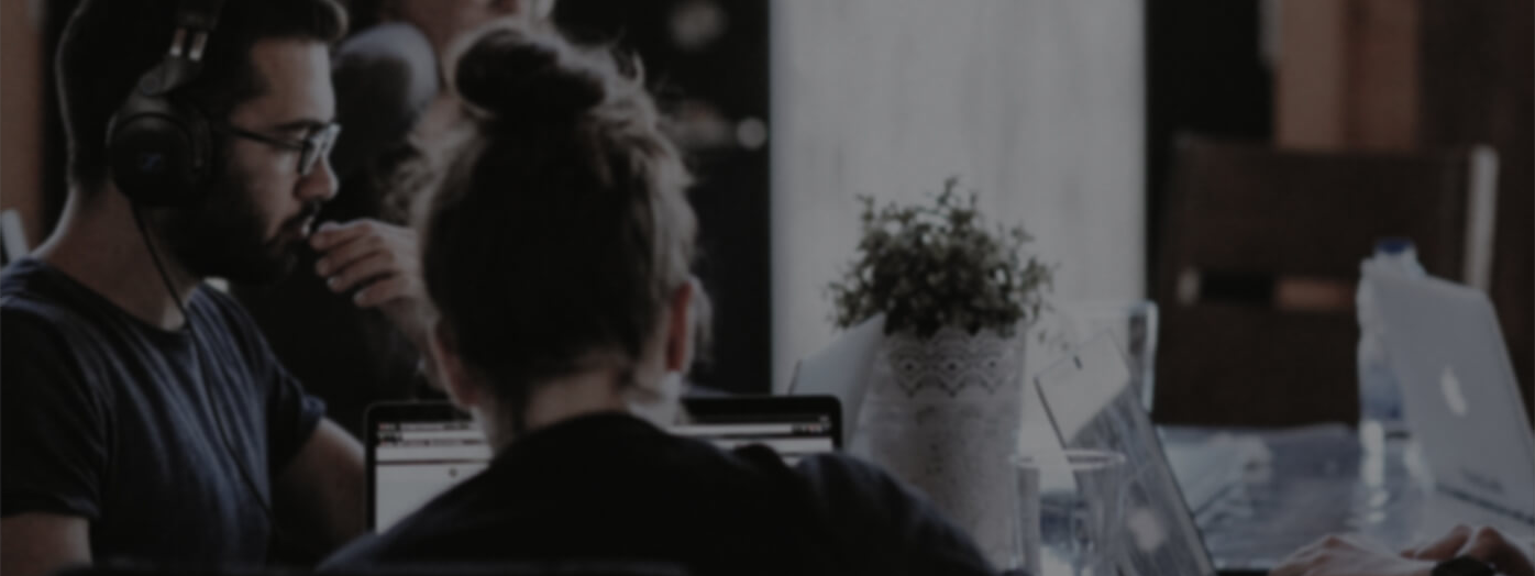 Ein Mann mit Kopfhörer auf den Ohren sitzt links an einem Tisch, davor mit dem Rücken zum Betrachter sitzt ein Mensch mit zusammengebundenen Haaren.