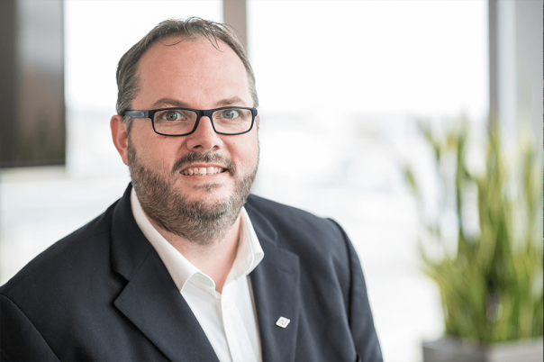 Ein Mann, der sich in einem Büro befindet und einen Anzug sowie eine Brille trägt.