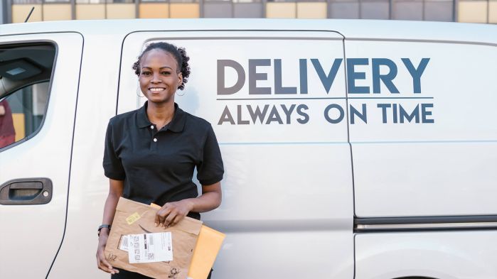 Eine Frau steht vor einem weißen Lieferwagen mit einem Paket.