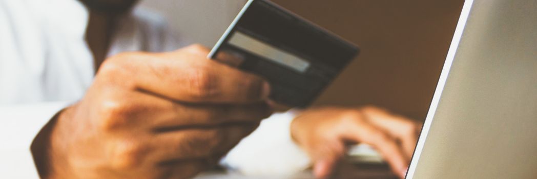 Man in white shirt types credit card data on his laptop while holding it in the other hand