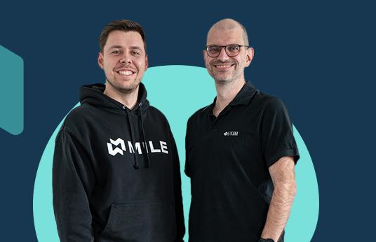 Ein blauer Hintergrund, auf dem Steffen Hauptmann und Stefan Seufert im Vordergrund abgebildet sind.