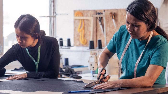 Mutter und Tochter nähen an einem Nähtisch ein Kleidungsstück.