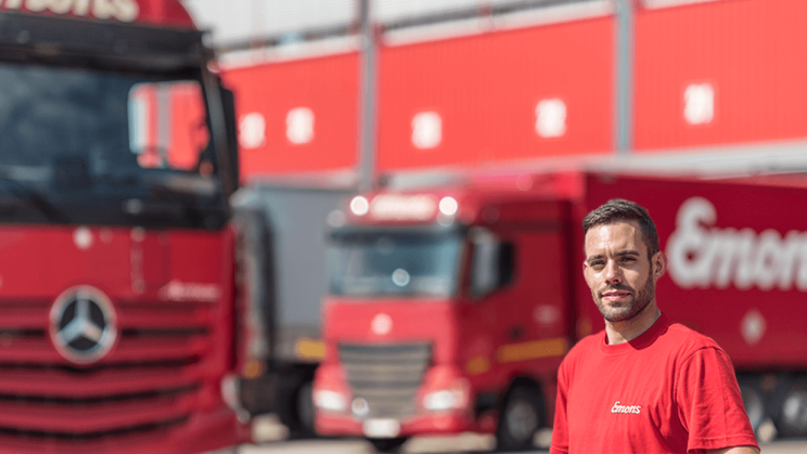 An Emons company employee can be seen in the foreground. Two red lorries can be seen in the background.