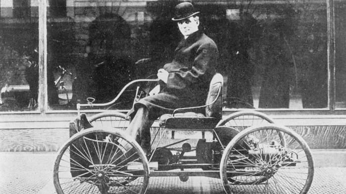 Schwarz-weiß-Foto von Henry Ford auf einem historischen Automodel