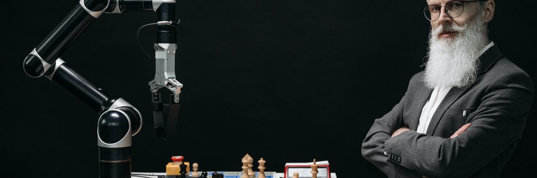 Older man with gray hair stands in a laboratory and plays chess against artificial intelligence