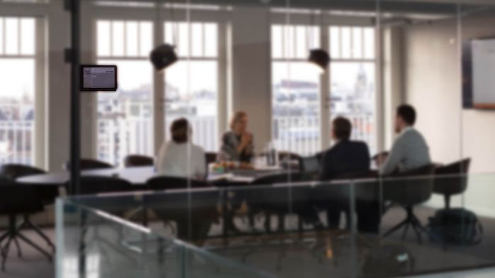 Employees sitting at meeting table in meeting room which is signposted with Wireless ePaper Display
