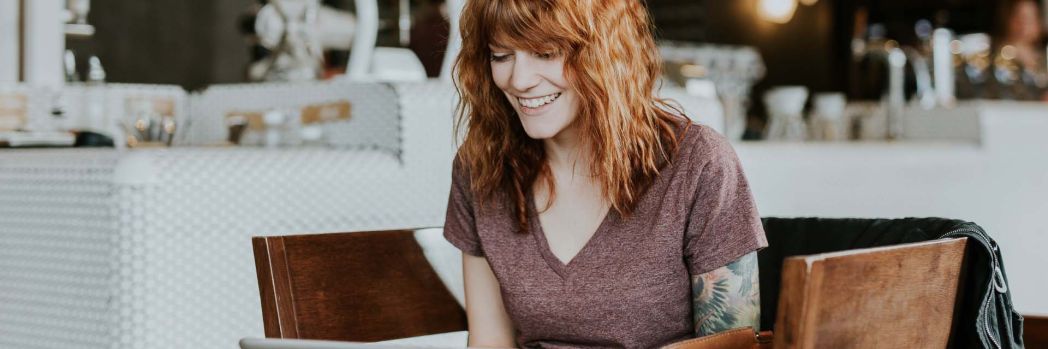 Frau mit roten Haaren sitzt an einem Tisch und arbeitet dank Desktop Virtualisierung mit ihrem Laptop im Cafe