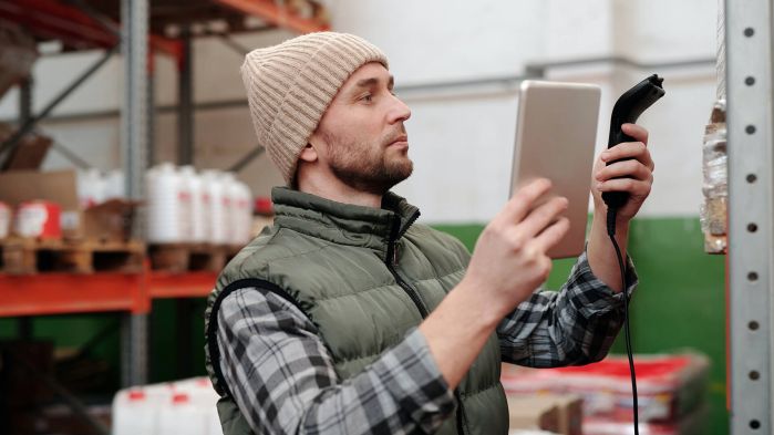 Mitarbeiter steht im Lager und nutzt digitale Software um Schäden an Versicherung zu melden.