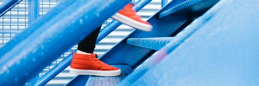 Person mit roten Schuhen läuft eine blaue Treppe in einer Lagerhalle hoch