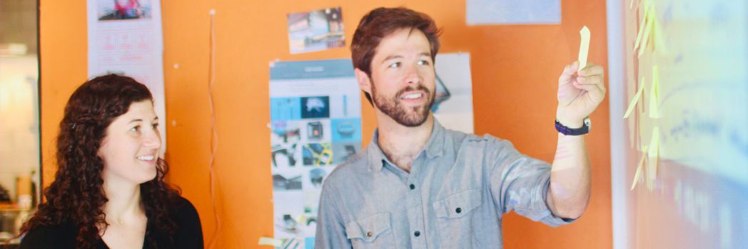 Man and woman standing at whiteboard smiling with post-it in hand