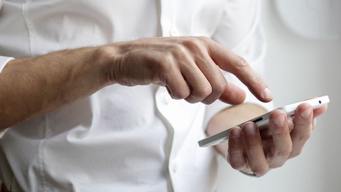 Mann im weißen Hemd tippt auf einem Smartphone