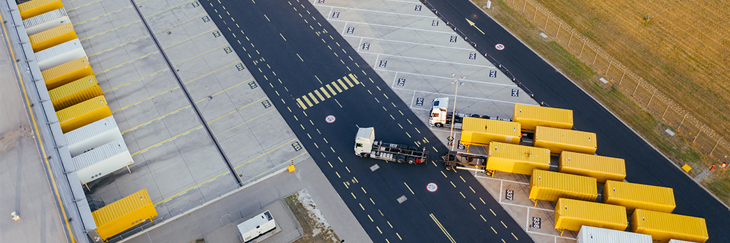 EIKONA Time Slot Management: Neue Features auf der LogiMAT 2023. Logistikgelände mit Hallen und gelben und weißen LKW.