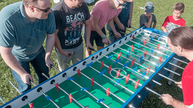 Mehrere Personen spielen Tischkicker gegeneinander.