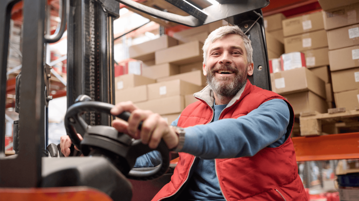 Ein Staplerfahrer bei der Arbeit, während der er lächelt.