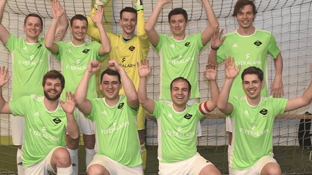 9 Personen stehen in einer Halle vor einem Tor.