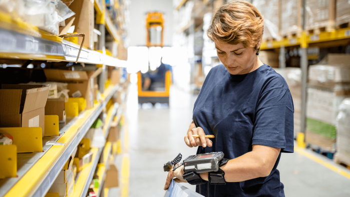 Lagermitarbeiterin nutzt WLAN in einer Lagerhalle, um ein mobiles Gerät zu bedienen.