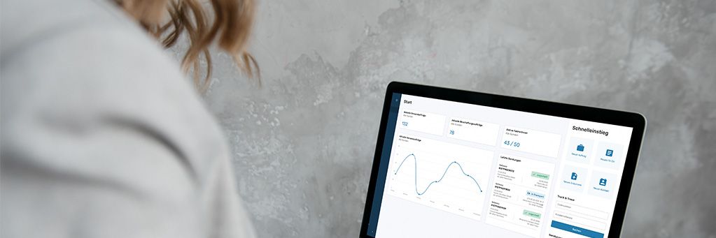 Eine Person betrachtet ein Laptop-Display mit einem Dashboard, das Diagramme und Statistiken zeigt, vor einer grauen Wand.