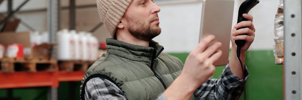 Mitarbeiter steht im Lager und nutzt digitale Software um Schäden an Versicherung zu melden.