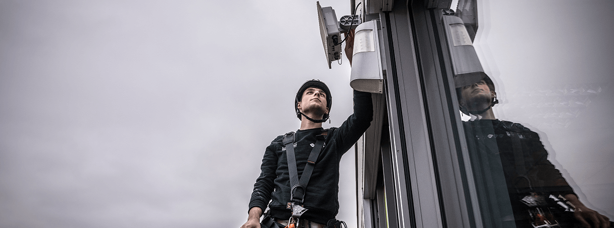 Eine Person montiert ein WLAN-Gerät an die Außenwand eines Gebäudes.