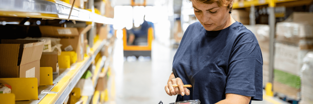 Lagermitarbeiterin nutzt WLAN in einer Lagerhalle, um ein mobiles Gerät zu bedienen.