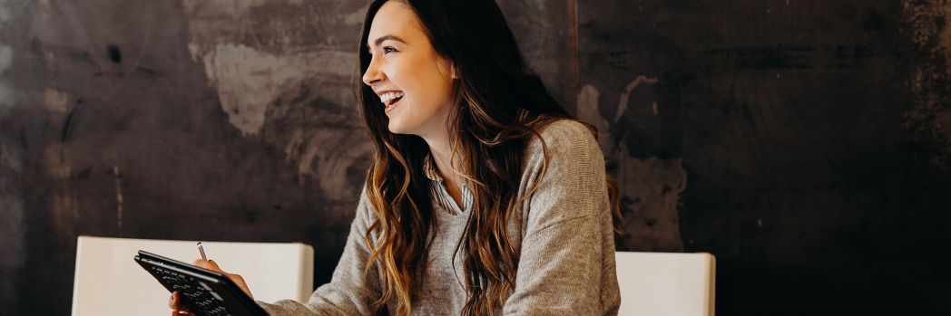 Woman with brown knitted sweater and tablet in hand smiles because of good customer service of shipping company