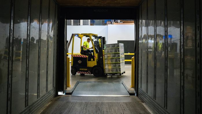 Employee drives through warehouse with loaded forklift, representing warehouse management systems and lower logistics costs