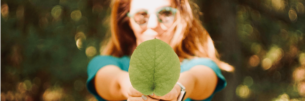 Frau in grünem T-Shirt hält grünes Blatt in die Kamera.