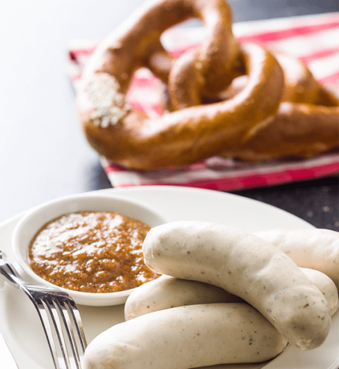 Weißwürste, Gabel und Senft auf einem weißen Teller.