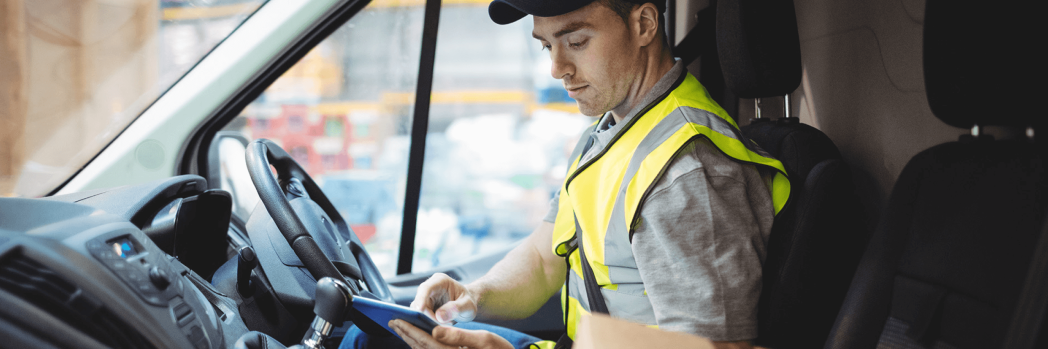 Ein Lieferfahrer in Warnweste nutzt ein Tablet im Lieferwagen, um Kommunikation effizient zu überbrücken.