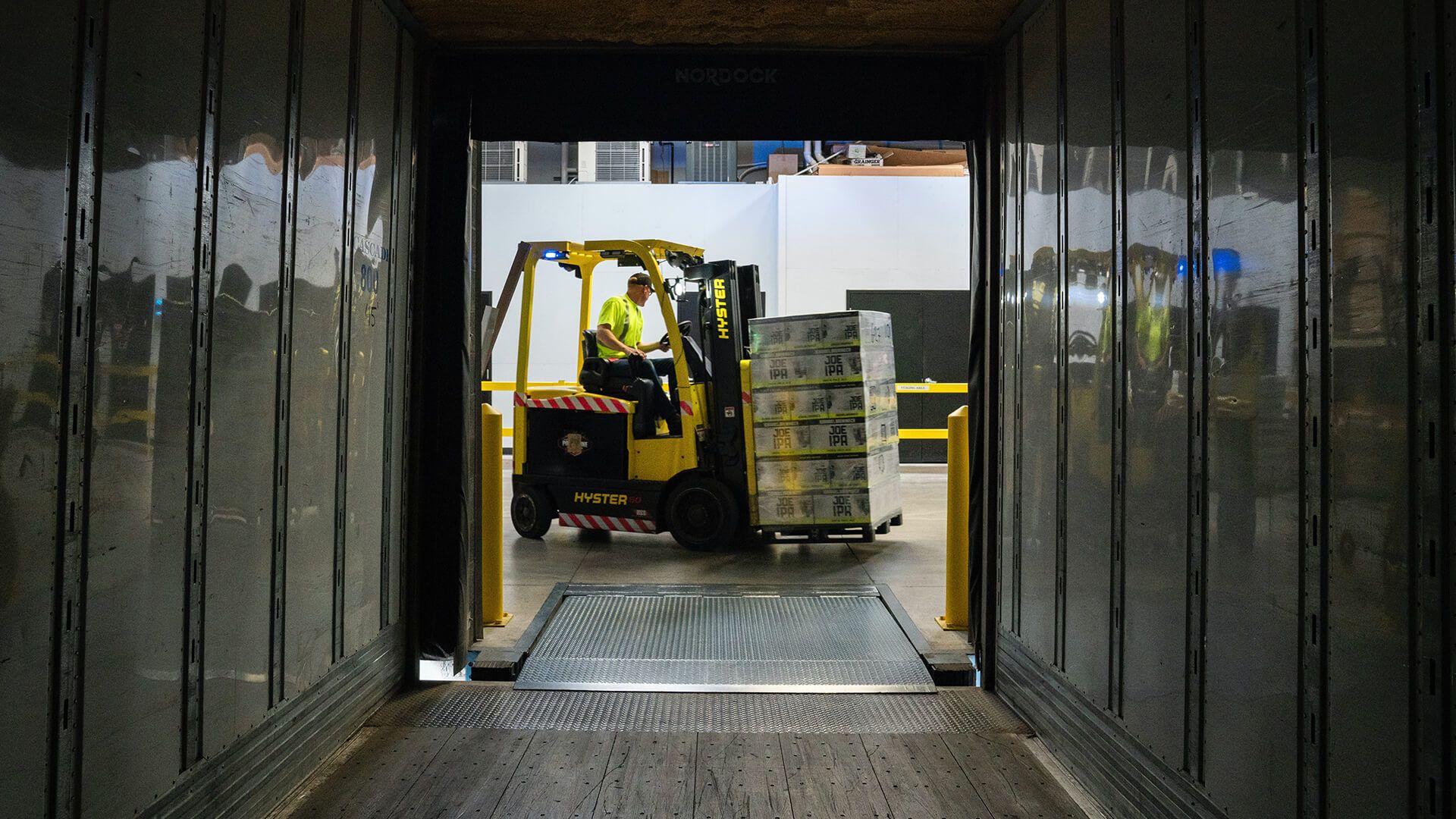 Mitarbeiter fährt mit beladenem Gabelstapler durch Lager, was für Lagerverwaltungssysteme und niedrigere Logistikkosten steht