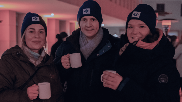 Drei Mitarbeiter von EIKONA Logistics sind im Vordergrund des Bildes zu sehen und halten ein Tasse in der Hand.