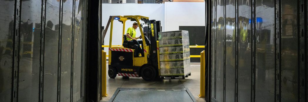Mitarbeiter fährt mit beladenem Gabelstapler durch Lager, was für Lagerverwaltungssysteme und niedrigere Logistikkosten steht